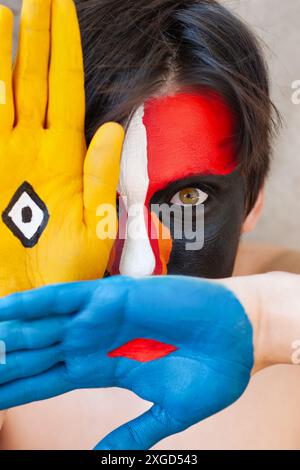 giovane con un volto dipinto, tenendo le mani di fronte a lui Foto Stock