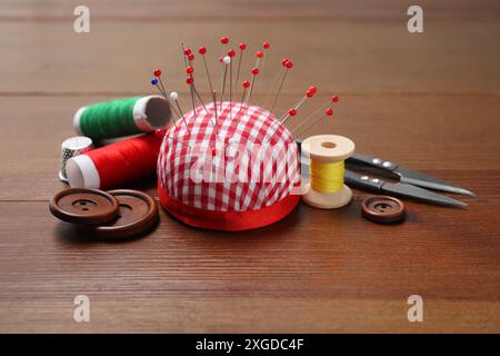 Cuscinetto a scacchi con perni da cucire, bobine di filettature, taglierina e bottoni su tavolo in legno Foto Stock