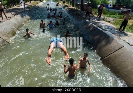 Kashmir, India. 8 luglio 2024. I residenti del Kashmir hanno visto nuotare in un canale d'acqua durante una giornata calda a Pulwama. Quest'anno il Kashmir ha affrontato sfide climatiche senza precedenti, segnate da temperature massime record a Srinagar e in tutta la regione. Gli esperti attribuiscono questi eventi meteorologici estremi agli impatti più ampi del cambiamento climatico. I cambiamenti nei modelli monsonici e la presenza irregolare di disturbi occidentali hanno interrotto i cicli meteorologici tradizionali della regione, portando a precipitazioni irregolari e fluttuazioni di temperatura. Credito: SOPA Images Limited/Alamy Live News Foto Stock