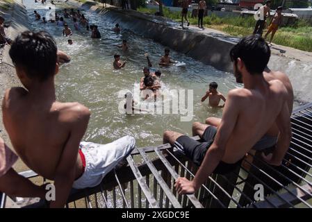 Kashmir, India. 8 luglio 2024. I residenti del Kashmir hanno visto nuotare in un canale d'acqua durante una giornata calda a Pulwama. Quest'anno il Kashmir ha affrontato sfide climatiche senza precedenti, segnate da temperature massime record a Srinagar e in tutta la regione. Gli esperti attribuiscono questi eventi meteorologici estremi agli impatti più ampi del cambiamento climatico. I cambiamenti nei modelli monsonici e la presenza irregolare di disturbi occidentali hanno interrotto i cicli meteorologici tradizionali della regione, portando a precipitazioni irregolari e fluttuazioni di temperatura. Credito: SOPA Images Limited/Alamy Live News Foto Stock