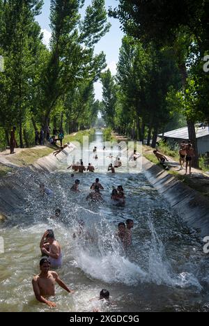 Kashmir, India. 8 luglio 2024. I residenti del Kashmir hanno visto nuotare in un canale d'acqua durante una giornata calda a Pulwama. Quest'anno il Kashmir ha affrontato sfide climatiche senza precedenti, segnate da temperature massime record a Srinagar e in tutta la regione. Gli esperti attribuiscono questi eventi meteorologici estremi agli impatti più ampi del cambiamento climatico. I cambiamenti nei modelli monsonici e la presenza irregolare di disturbi occidentali hanno interrotto i cicli meteorologici tradizionali della regione, portando a precipitazioni irregolari e fluttuazioni di temperatura. Credito: SOPA Images Limited/Alamy Live News Foto Stock