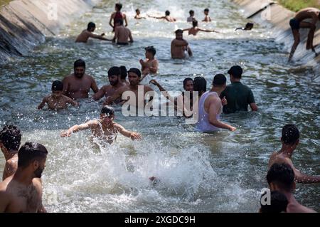 Kashmir, India. 8 luglio 2024. I residenti del Kashmir hanno visto nuotare in un canale d'acqua durante una giornata calda a Pulwama. Quest'anno il Kashmir ha affrontato sfide climatiche senza precedenti, segnate da temperature massime record a Srinagar e in tutta la regione. Gli esperti attribuiscono questi eventi meteorologici estremi agli impatti più ampi del cambiamento climatico. I cambiamenti nei modelli monsonici e la presenza irregolare di disturbi occidentali hanno interrotto i cicli meteorologici tradizionali della regione, portando a precipitazioni irregolari e fluttuazioni di temperatura. Credito: SOPA Images Limited/Alamy Live News Foto Stock