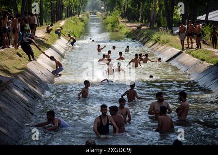 Kashmir, India. 8 luglio 2024. I residenti del Kashmir hanno visto nuotare in un canale d'acqua durante una giornata calda a Pulwama. Quest'anno il Kashmir ha affrontato sfide climatiche senza precedenti, segnate da temperature massime record a Srinagar e in tutta la regione. Gli esperti attribuiscono questi eventi meteorologici estremi agli impatti più ampi del cambiamento climatico. I cambiamenti nei modelli monsonici e la presenza irregolare di disturbi occidentali hanno interrotto i cicli meteorologici tradizionali della regione, portando a precipitazioni irregolari e fluttuazioni di temperatura. Credito: SOPA Images Limited/Alamy Live News Foto Stock