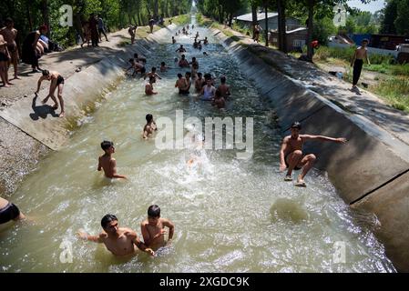 Kashmir, India. 8 luglio 2024. I residenti del Kashmir hanno visto nuotare in un canale d'acqua durante una giornata calda a Pulwama. Quest'anno il Kashmir ha affrontato sfide climatiche senza precedenti, segnate da temperature massime record a Srinagar e in tutta la regione. Gli esperti attribuiscono questi eventi meteorologici estremi agli impatti più ampi del cambiamento climatico. I cambiamenti nei modelli monsonici e la presenza irregolare di disturbi occidentali hanno interrotto i cicli meteorologici tradizionali della regione, portando a precipitazioni irregolari e fluttuazioni di temperatura. Credito: SOPA Images Limited/Alamy Live News Foto Stock