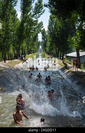 I residenti del Kashmir hanno visto nuotare in un canale d'acqua durante una giornata calda a Pulwama. Quest'anno il Kashmir ha affrontato sfide climatiche senza precedenti, segnate da temperature massime record a Srinagar e in tutta la regione. Gli esperti attribuiscono questi eventi meteorologici estremi agli impatti più ampi del cambiamento climatico. I cambiamenti nei modelli monsonici e la presenza irregolare di disturbi occidentali hanno interrotto i cicli meteorologici tradizionali della regione, portando a precipitazioni irregolari e fluttuazioni di temperatura. Questi cambiamenti non solo influenzano i modelli agricoli e le risorse idriche, ma anche pongono segni Foto Stock