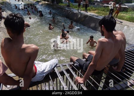 I residenti del Kashmir hanno visto nuotare in un canale d'acqua durante una giornata calda a Pulwama. Quest'anno il Kashmir ha affrontato sfide climatiche senza precedenti, segnate da temperature massime record a Srinagar e in tutta la regione. Gli esperti attribuiscono questi eventi meteorologici estremi agli impatti più ampi del cambiamento climatico. I cambiamenti nei modelli monsonici e la presenza irregolare di disturbi occidentali hanno interrotto i cicli meteorologici tradizionali della regione, portando a precipitazioni irregolari e fluttuazioni di temperatura. Questi cambiamenti non solo influenzano i modelli agricoli e le risorse idriche, ma anche pongono segni Foto Stock