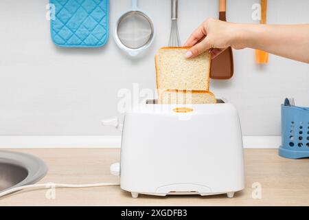 mano di donna che mette il pane nel tostapane. casalinga che frigge il pane in un tostapane, in cucina. donna che fa un brindisi. tostare il pane in un tostapane. un piec Foto Stock