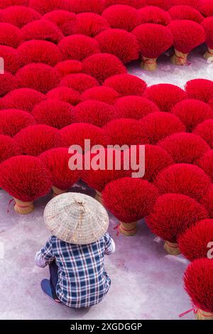 L'incenso rosso vibrante è disposto a terra per asciugare al sole a Quang Phu Cau, Ung Hoa, Vietnam del Nord, Asia a giugno - bastoncini di incenso rosso donna Foto Stock