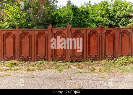 Porta del giardino trascurata con pannelli metallici arrugginiti, ampio cancello di recinzione rurale Foto Stock