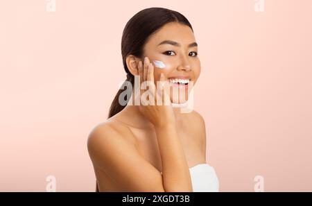 Concetto di bellezza. Donna asiatica di applicare una crema idratante sul viso Foto Stock