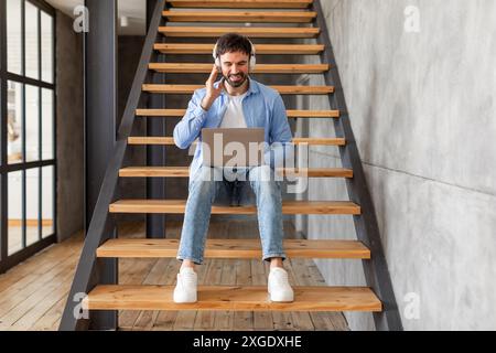 Uomo che utilizza un laptop seduto su scale interne Foto Stock