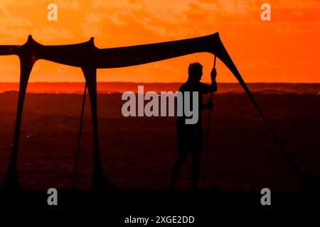 Isola di Palms, Stati Uniti. 8 luglio 2024. Un beachgoer sagomato dall'alba, assembla un'ombra lungo la spiaggia di Wild Dunes, 8 luglio 2024, a Isle of Palms, South Carolina. Si prevede che la corsa del clima estremamente caldo e umido continuerà nonostante i temporali che si spostano nella regione. Crediti: Richard Ellis/Richard Ellis/Alamy Live News Foto Stock