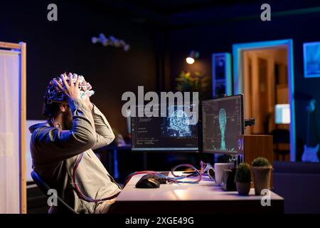 Scienziato informatico che posiziona le cuffie EEG sulla testa per comunicare con l'entità dell'intelligenza artificiale con corpo antropomorfo. Professionista IT che utilizza attrezzature high-tech per parlare con robot ai in forma umanoide Foto Stock
