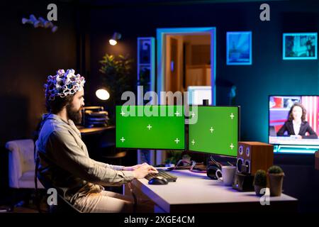 Ingegnere del software con auricolare EEG che inizia a caricare la mente su una configurazione multi-monitor a schermo isolato, cercando di ottenere poteri bionici. Esperto IT che utilizza attrezzature neuroscientifiche ad alta tecnologia e un PC desktop mockup Foto Stock