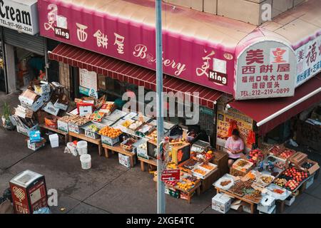 Un proprietario di un negozio di alimentari cinese espone frutta e verdura sulla strada di Chinatown, New York, mentre un autista di consegna attende nelle vicinanze Foto Stock