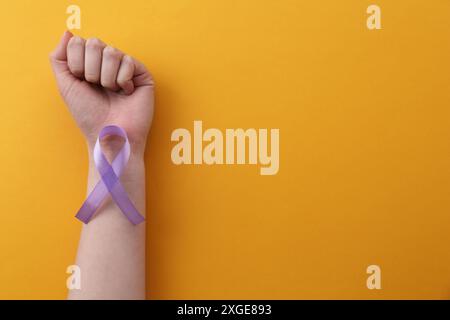 Donna con nastro di sensibilizzazione viola su sfondo arancione, vista dall'alto. Spazio per il testo Foto Stock