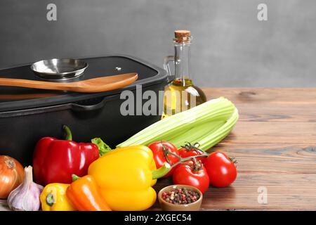 Pentola nera con coperchio in vetro, prodotti diversi e cucchiaio su tavolo in legno Foto Stock