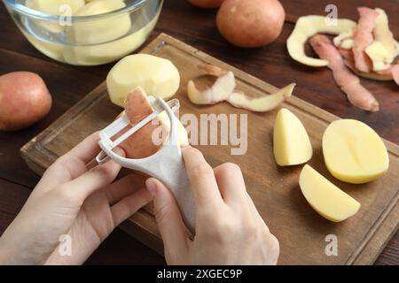 Donna che sbuccia patate fresche con pelapatate al tavolo di legno Foto Stock