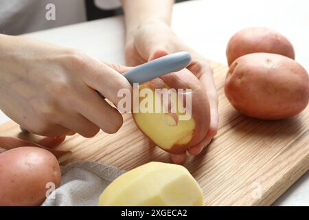 Donna che sbuccia patate fresche con pelapatate a tavola, primo piano Foto Stock