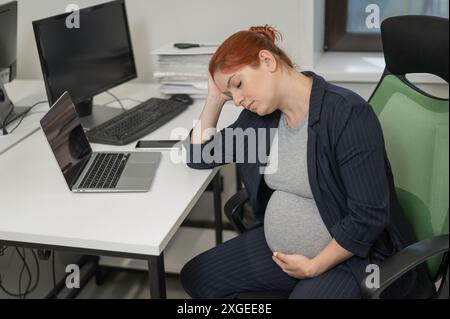 Donna incinta che dorme alla sua scrivania in ufficio. Foto Stock