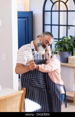 Ballare insieme, una coppia anziana che indossa grembiuli che condivide un momento tenero in cucina Foto Stock