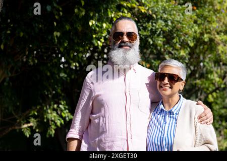 Coppia senior che indossa occhiali da sole, sorride e abbraccia all'aperto alla luce del sole Foto Stock