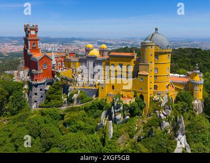 Magnifico castello con torri colorate ed edifici in un verde paesaggio collinare sotto un cielo blu, vista aerea, Palacio Nacional da pena, Nazionale Foto Stock