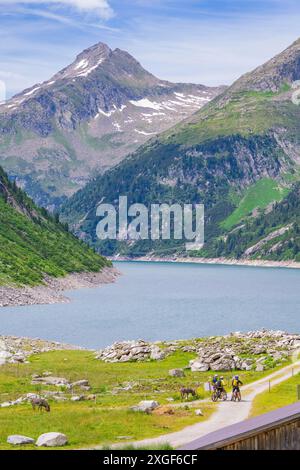 Vista di un lago di montagna con ciclisti su un sentiero, natura verde e cielo blu, Klein Tibet, Zillertal, Austria Foto Stock