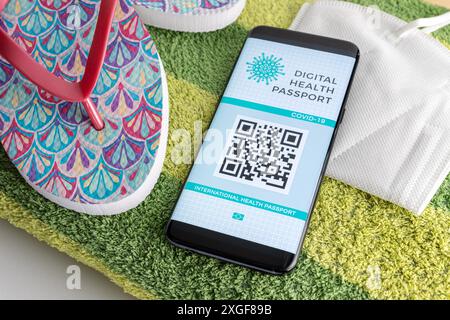 Smartphone con Digital Health o passaporto di vaccinazione sullo schermo, KN95 maschera facciale e alcuni accessori da spiaggia. Passaporto COVID-19 per viaggiare in data Foto Stock