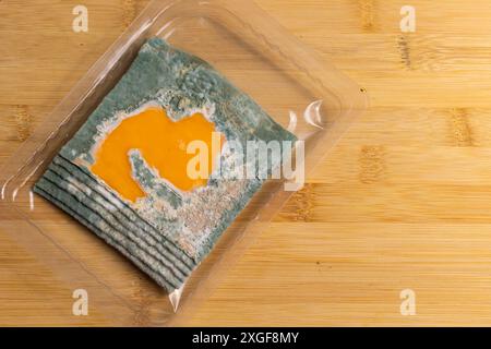Fette di formaggio giallo ammuffito disposte su un tagliere di bambù. Spore di muffa verdi sul cibo. Cibo sprecato scaduto Foto Stock