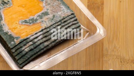 Fette di formaggio giallo ammuffito disposte su un tagliere di bambù. Spore di muffa verdi sul cibo. Cibo sprecato scaduto Foto Stock