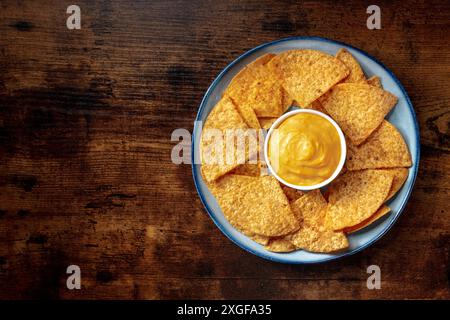 Nachos, patatine di tortilla messicane, sparate dall'alto su uno sfondo di legno con una salsa al formaggio Foto Stock