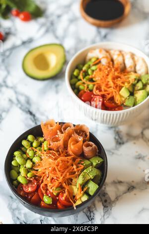 Deliziose ciotole con avocado, edamame, pomodori ciliegini, carote grattugiate, gamberetti, salmone e salsa di soia. Concetto di cibo sano Foto Stock