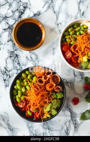 Vista dall'alto di due deliziosi e nutrienti poke ciotole con gamberi, salmone, edamame, carote, avocado, pomodori ciliegini, sesamo e salsa di soia su una biglia Foto Stock