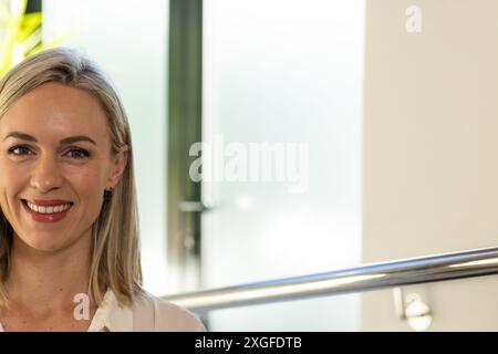 Donna sorridente in clinica medica, in piedi vicino alle ringhiere, guardando la macchina fotografica, copia spazio Foto Stock