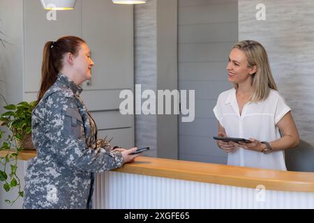 Soldato militare donna che parla con il receptionist tenendo tablet presso la clinica medica Foto Stock