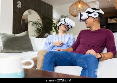 Utilizzando occhiali VR, coppie gay che ridono e si godono la realtà virtuale a casa Foto Stock