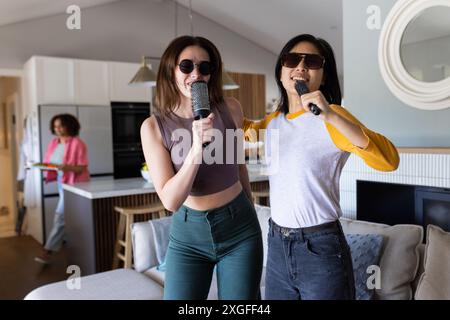 Cantare karaoke, due donne amiche con microfoni si divertono insieme a casa Foto Stock