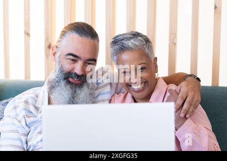 Sorridente coppia anziana che usa il laptop mentre si siede sul divano, divertendosi insieme Foto Stock