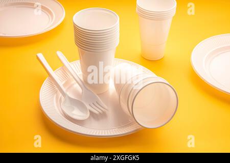 Rifiuti di stoviglie in plastica monouso. Gruppo di piatti, tazze, cucchiai, forchette e utensili vuoti su tavola gialla Foto Stock