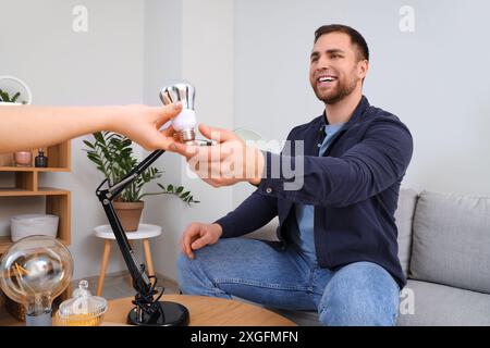 Giovane uomo che prende la lampadina per la lampada da scrivania di una donna a casa Foto Stock