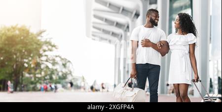 Coppia felice che cammina con i bagagli fuori dall'edificio moderno Foto Stock