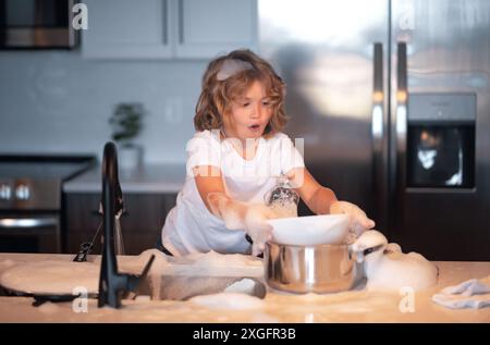 Simpatici ragazzi gemelli che aiutano in cucina a lavare i piatti. Bambini che si divertono con i lavori domestici. Piccola governante. Lavare e asciugare i piatti per bambini Foto Stock