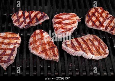 Numerose bistecche ben condite sfrigolano alla perfezione su un barbecue ardito Foto Stock