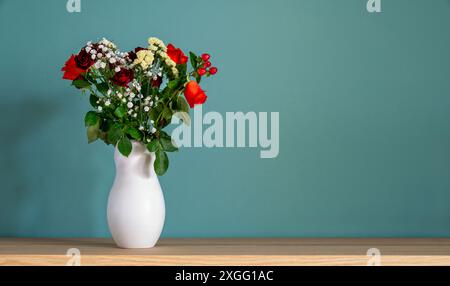 Bouquet di rose colorate in un vaso bianco su un tavolo di legno contro una parete turchese con spazio per le copie Foto Stock