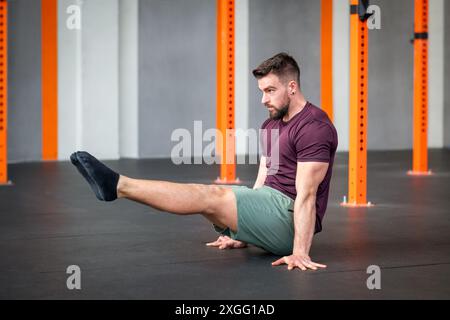 Corpo di un giovane e determinato uomo in abbigliamento sportivo che allunga le gambe mentre pratica la calistenica L SIT durante la lezione di fitness presso il centro fitness Foto Stock