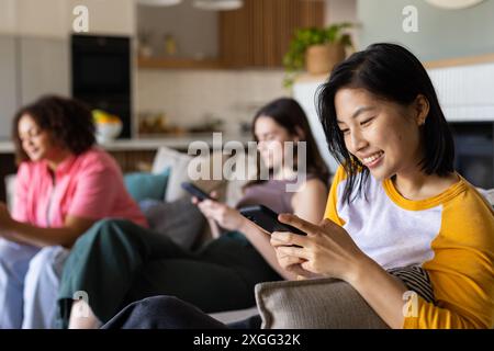 Utilizzando smartphone, tre donne e amici si rilassano sul divano in salotto Foto Stock