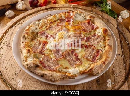 Pizza con pancetta fatta in casa circondata da ingredienti freschi su un tavolo da cucina in legno Foto Stock