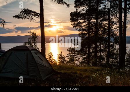 tenda turistica sulla riva di un lago forestale sullo sfondo di un pittoresco tramonto Foto Stock