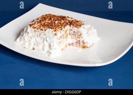 Delizioso dessert fatto in casa con una fetta parzialmente mangiata, rivelando il suo interno a strati servito su un piatto bianco incontaminato contro un profondi corteccia blu Foto Stock